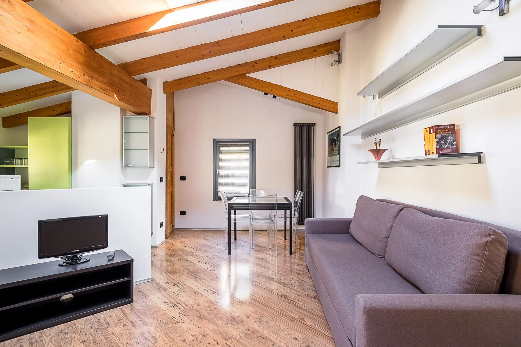 Una sala luminosa con sofá, televisor y mesa de comedor bajo vigas de madera.