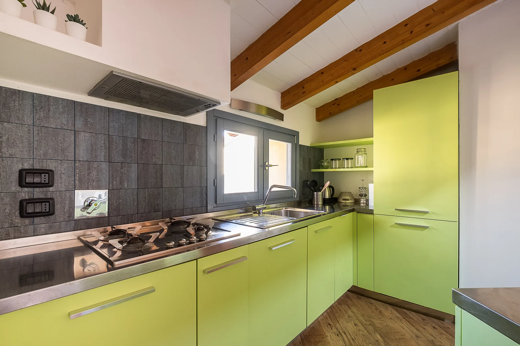 Una cocina luminosa con gabinetes verde lima, una placa de cocción y vigas de madera a la vista.