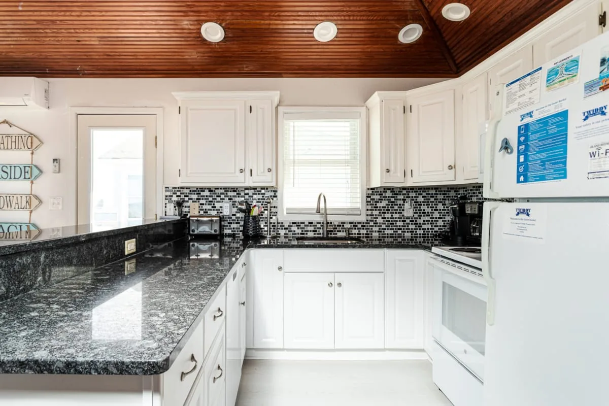 A bright kitchen with white cabinets, dark countertops, and a patterned backsplash.