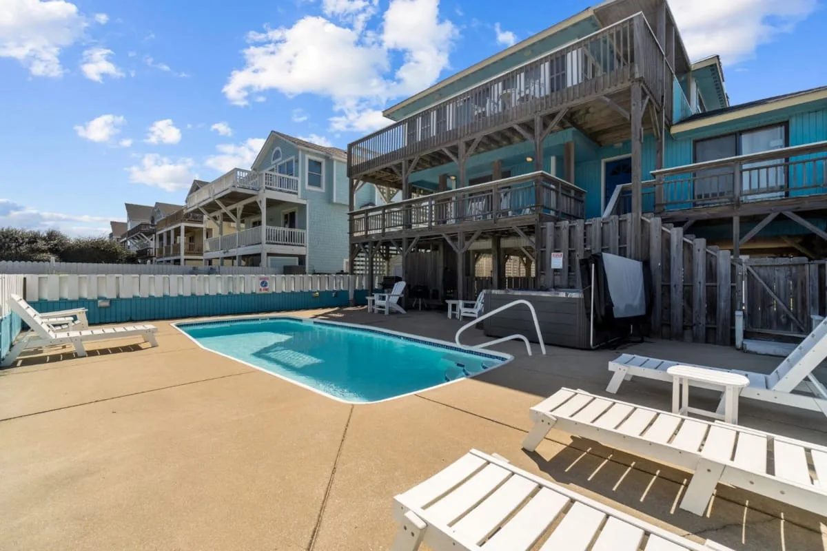A swimming pool sits beside a deck with lounge chairs and elevated coastal houses.