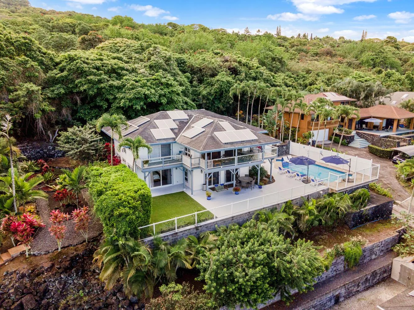 Una casa moderna y una piscina están rodeadas de vegetación frondosa en una ladera.