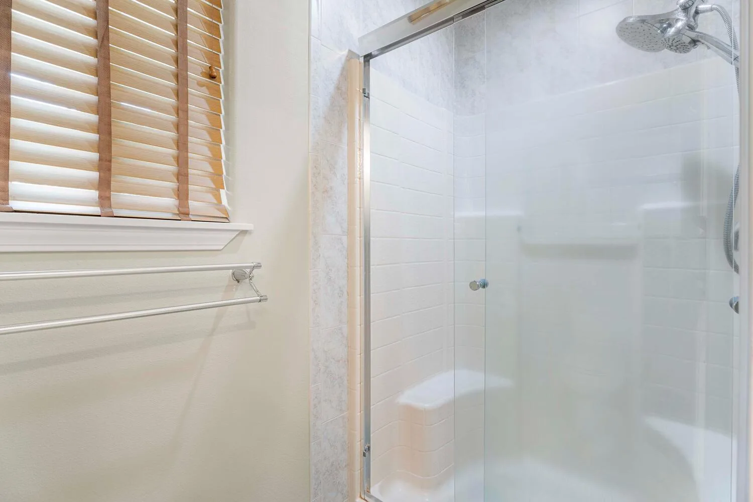 Un baño luminoso con una ducha de vidrio y una ventana con persianas de madera.