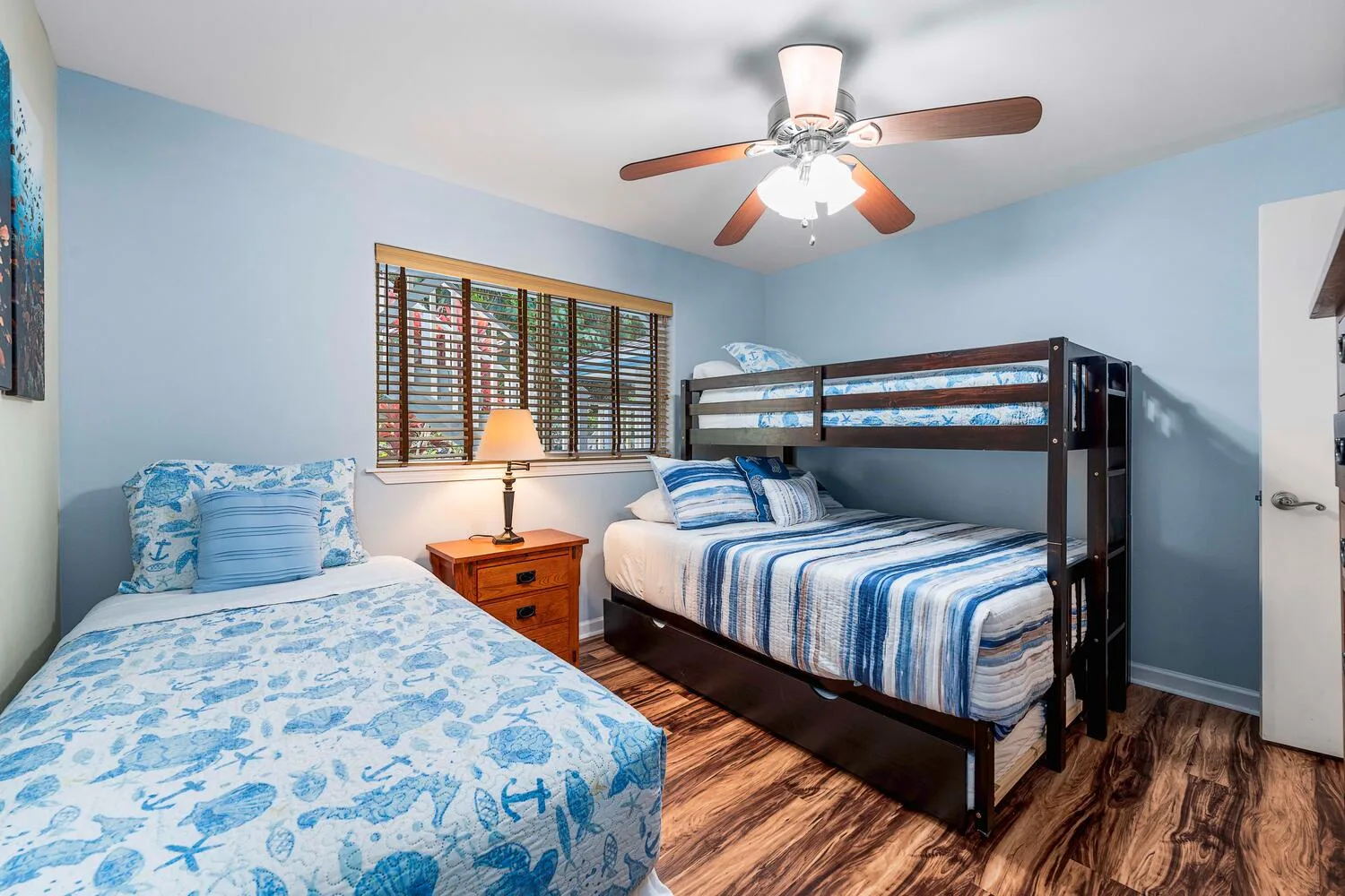 Un dormitorio con dos camas, ropa de cama azul y una ventana con persianas de madera.