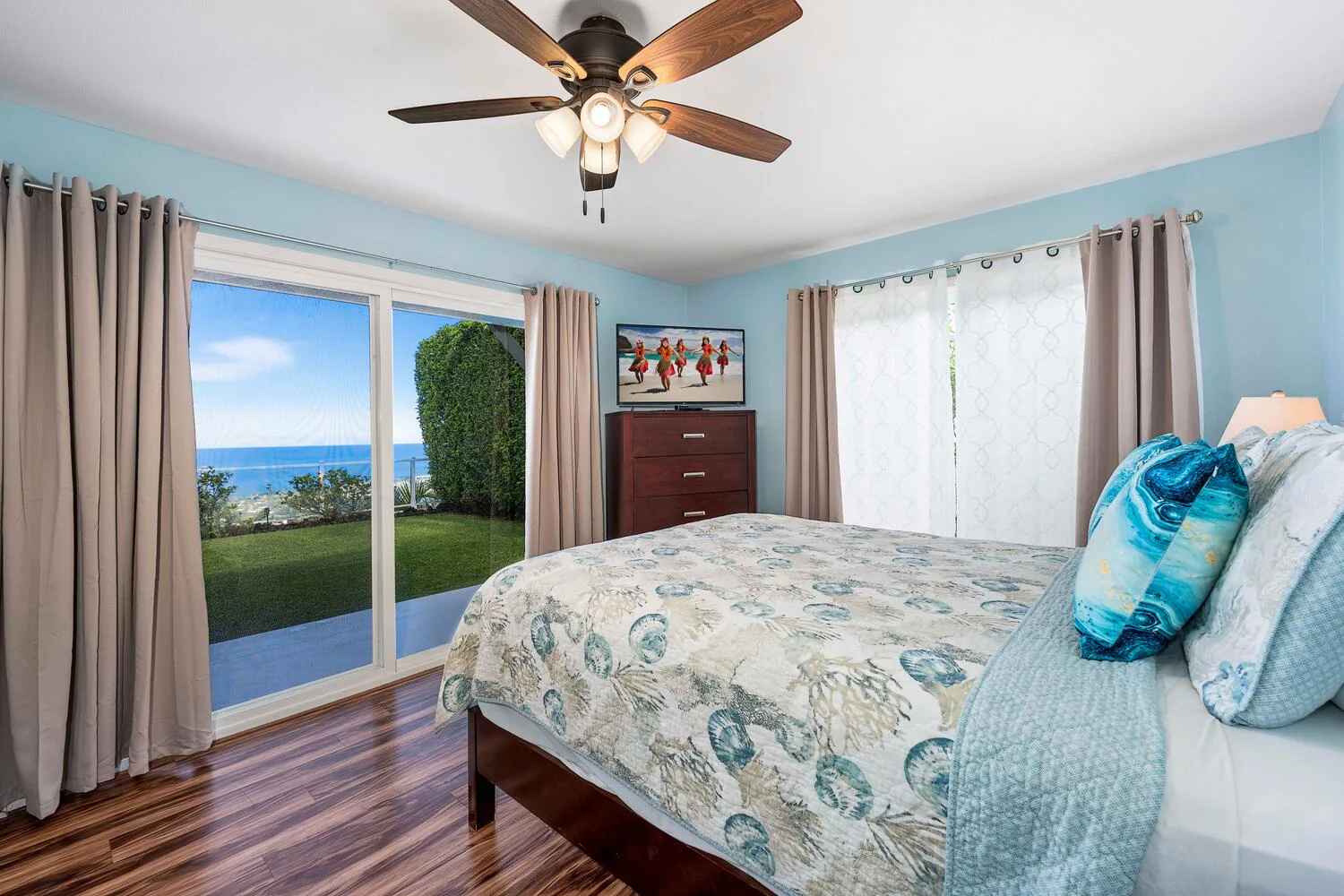 Un dormitorio con una colcha estampada, paredes azules y ventanas grandes.