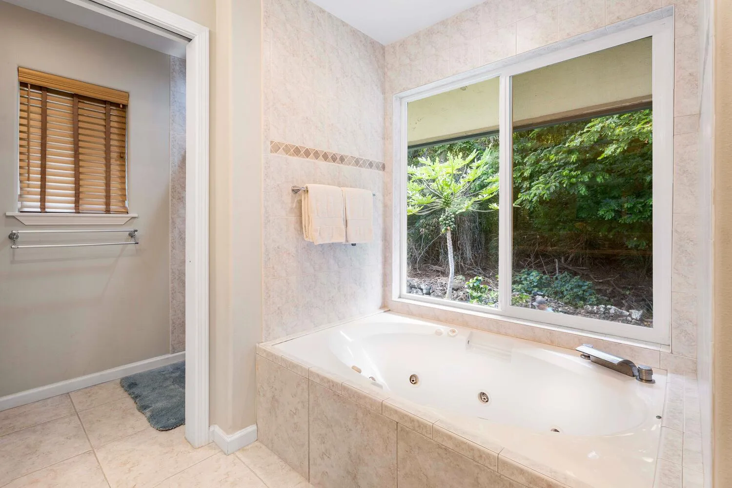 Un baño con una bañera bajo una ventana grande con vegetación a la vista.