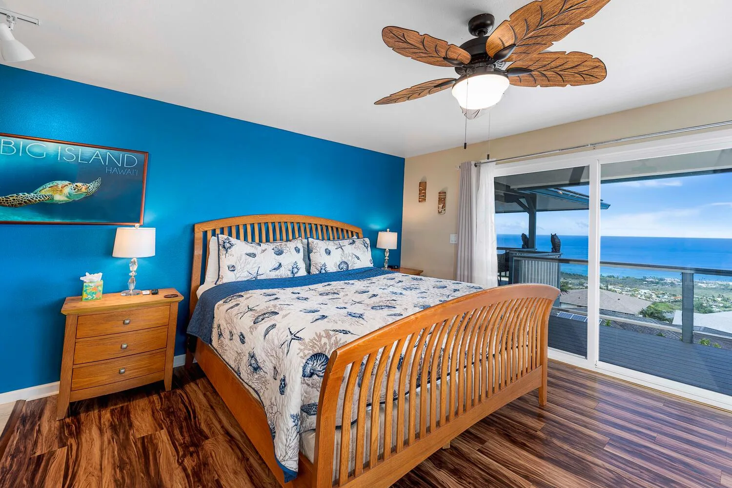 Un dormitorio con cama de madera, paredes azules y puertas corredizas de vidrio con vista al agua.