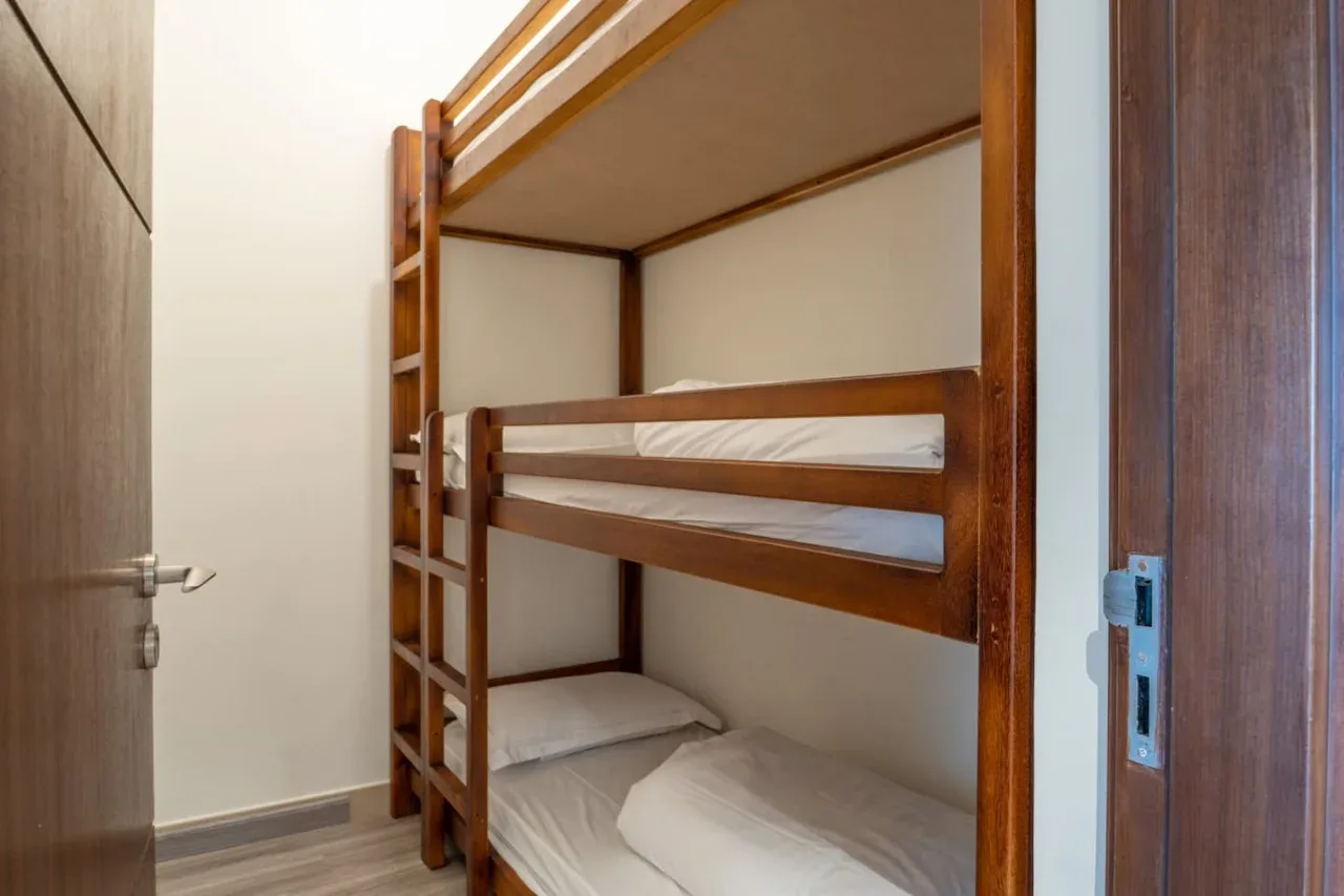 A bedroom with wooden bunk beds and white bedding.