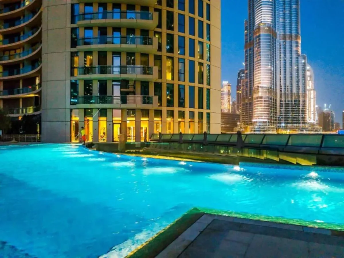 A rooftop pool overlooks illuminated high-rise buildings at night.