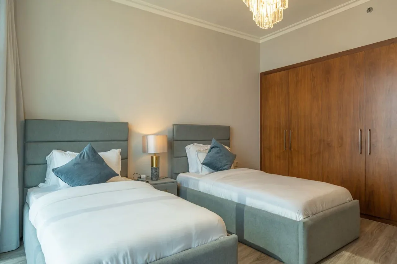 A bedroom with two beds, bedside lamps, and wooden wardrobes.