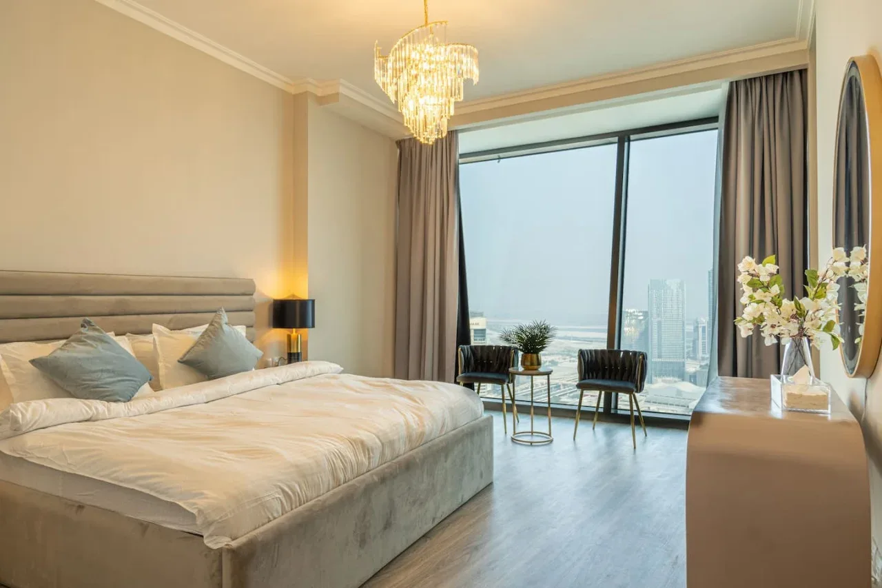 A bedroom with a large bed and floor-to-ceiling windows overlooking the city.
