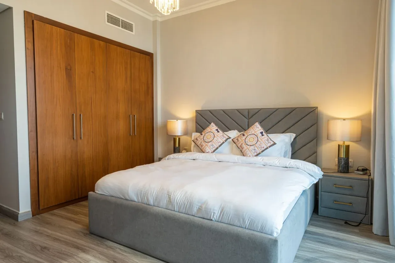A bedroom with a neatly made bed, bedside tables, and a wooden wardrobe.