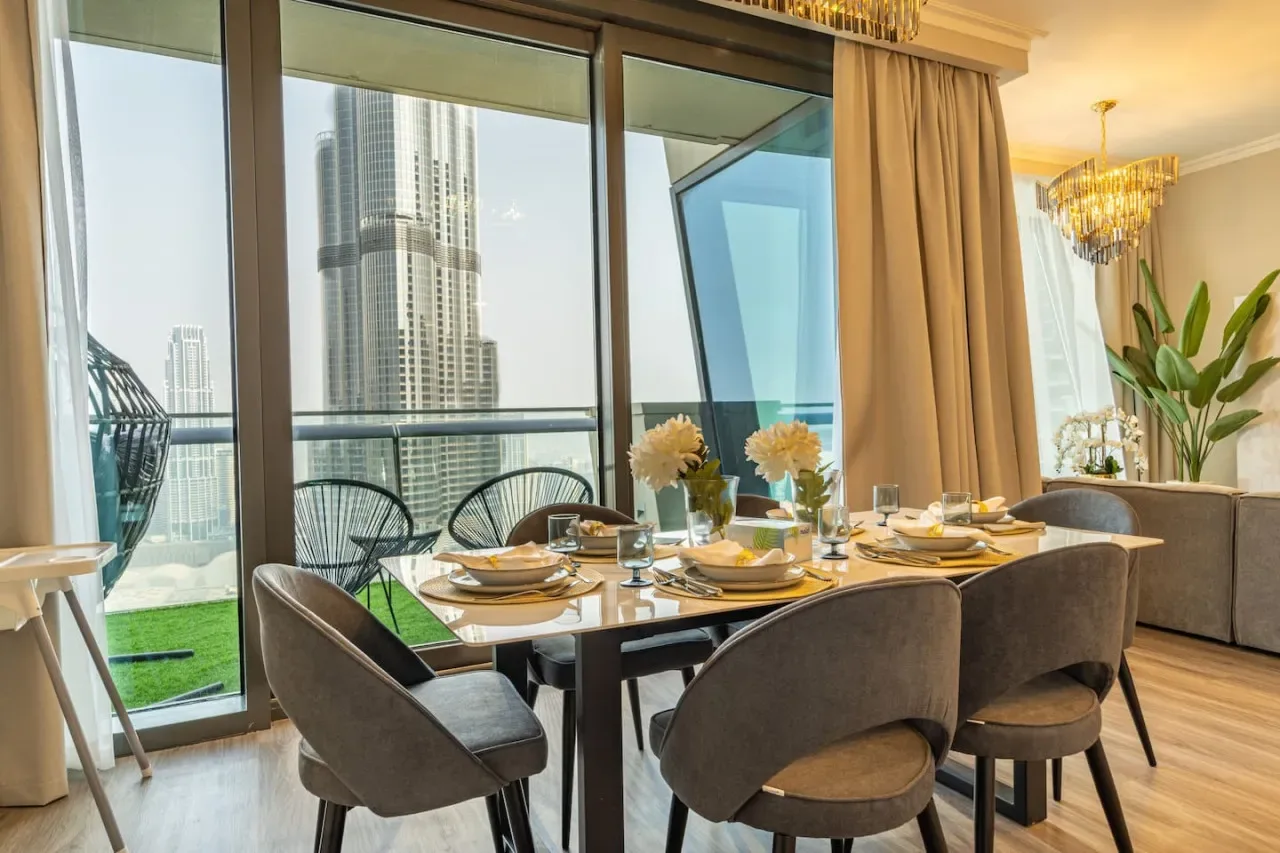 A dining area with a set table beside large windows overlooking nearby buildings.