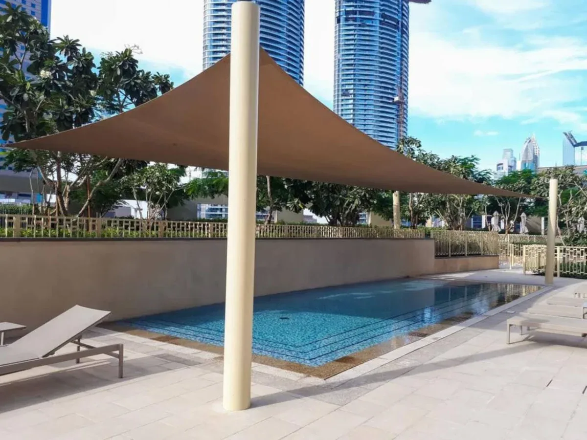 An outdoor swimming pool sits beneath a shade canopy, with lounge seating nearby.