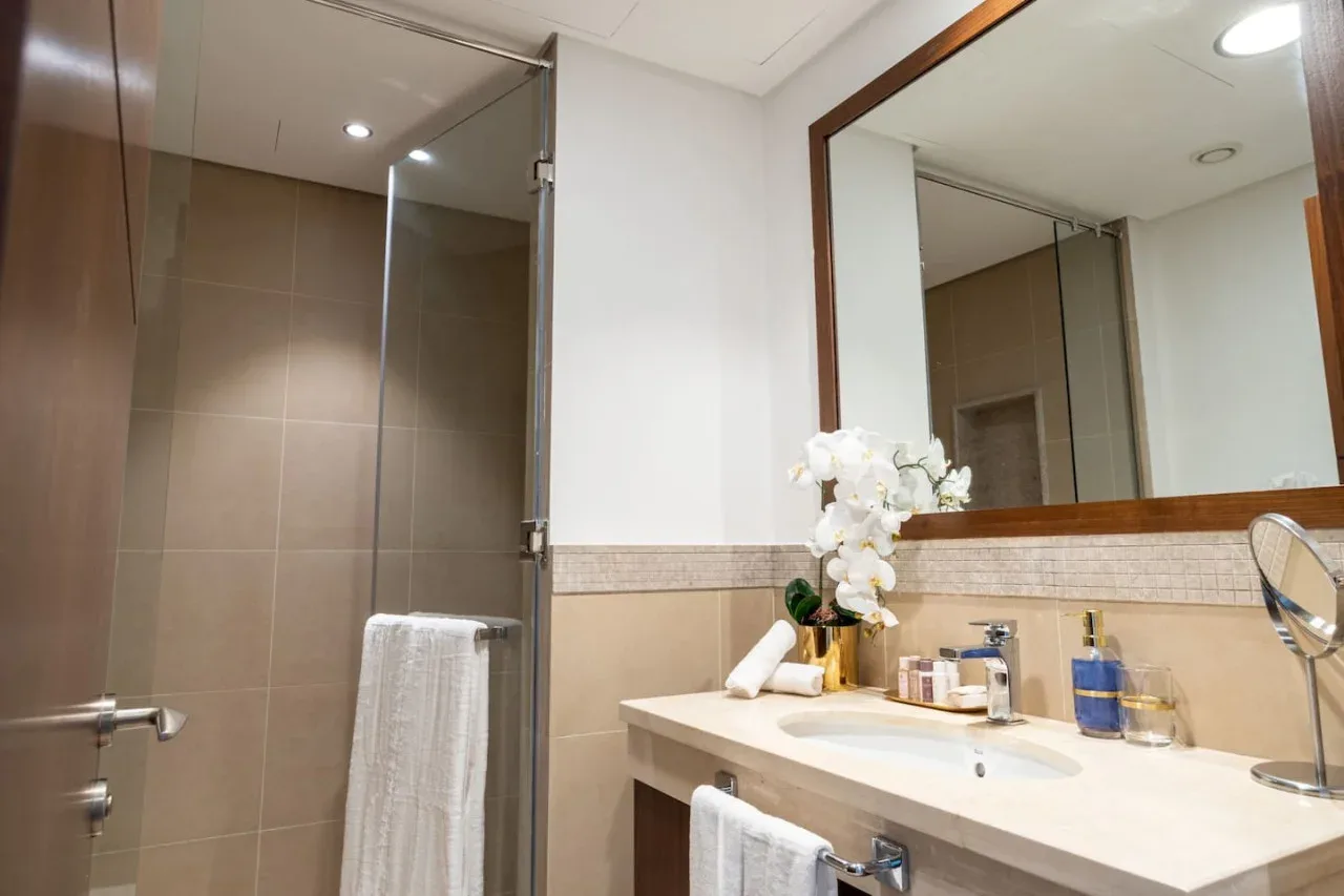 A bathroom vanity with a sink and mirror sits beside a glass shower.