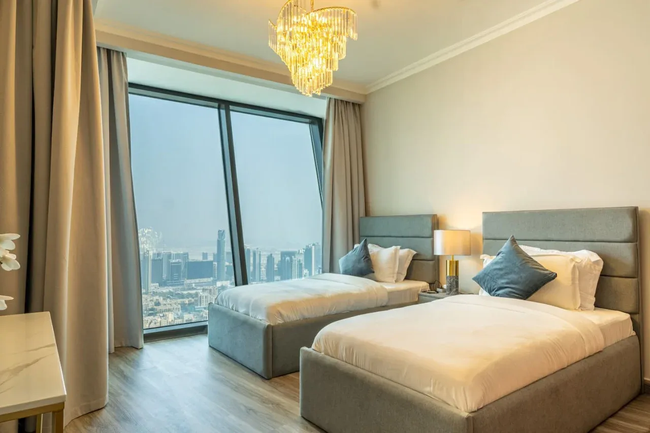 A bedroom with two beds beside large windows overlooking the city.