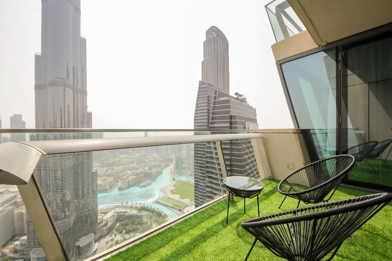 A balcony with outdoor seating overlooks a city skyline and turquoise water.