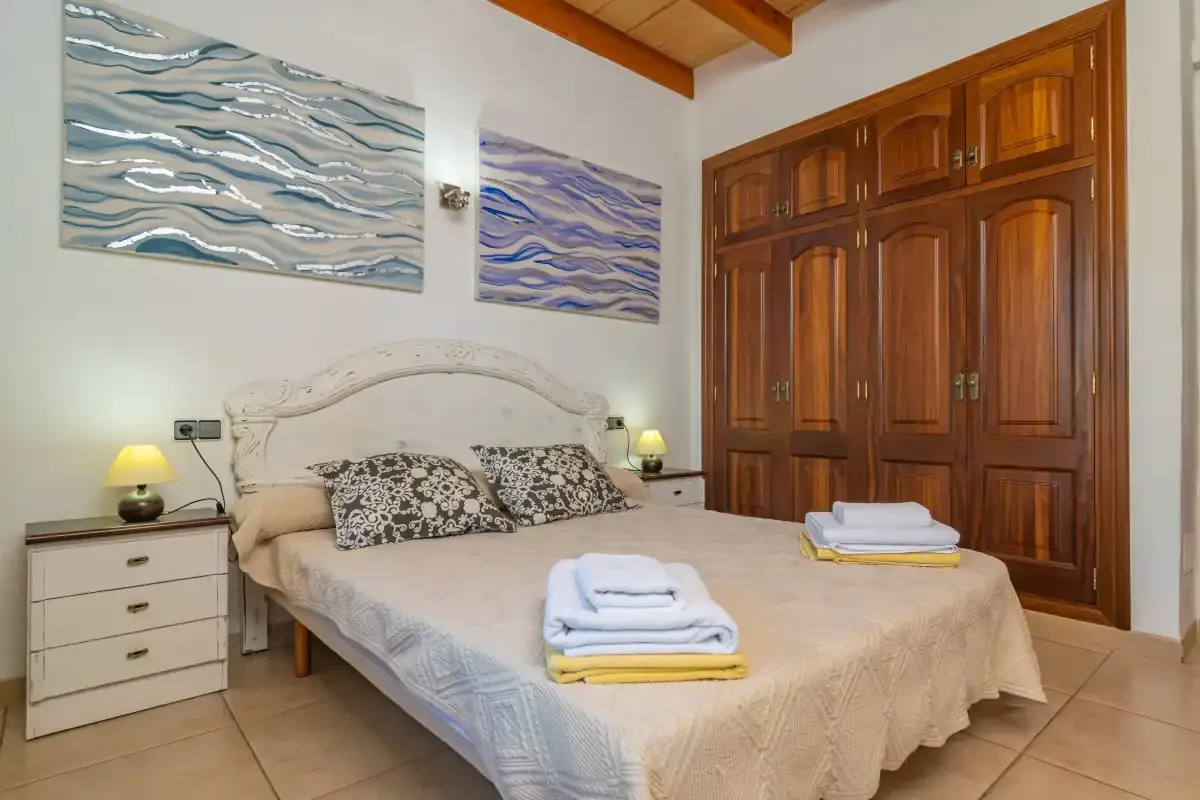 A bedroom with a double bed, bedside tables, and a large wooden wardrobe.