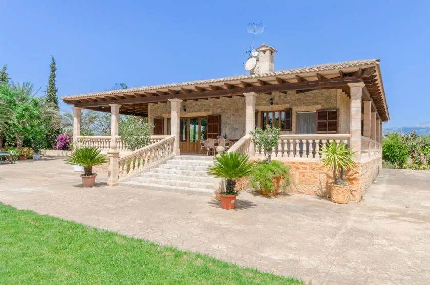 A stone house with a covered porch, broad steps, and potted plants.