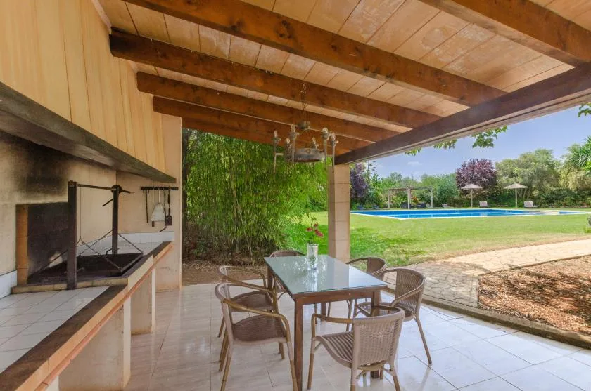 A covered outdoor dining area opens onto a lawn and swimming pool.