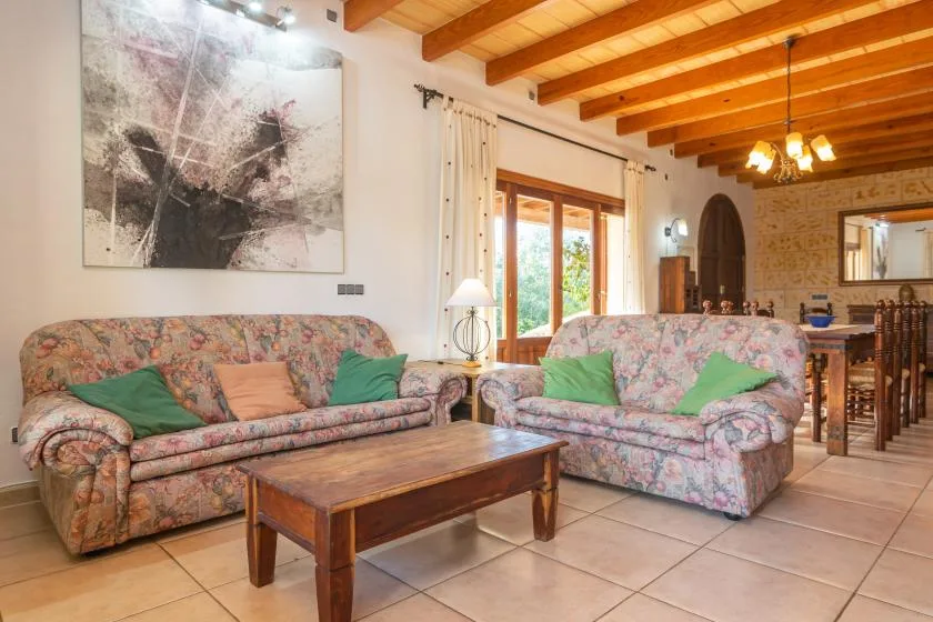 A living room with floral seating, a wooden coffee table, and exposed ceiling beams.