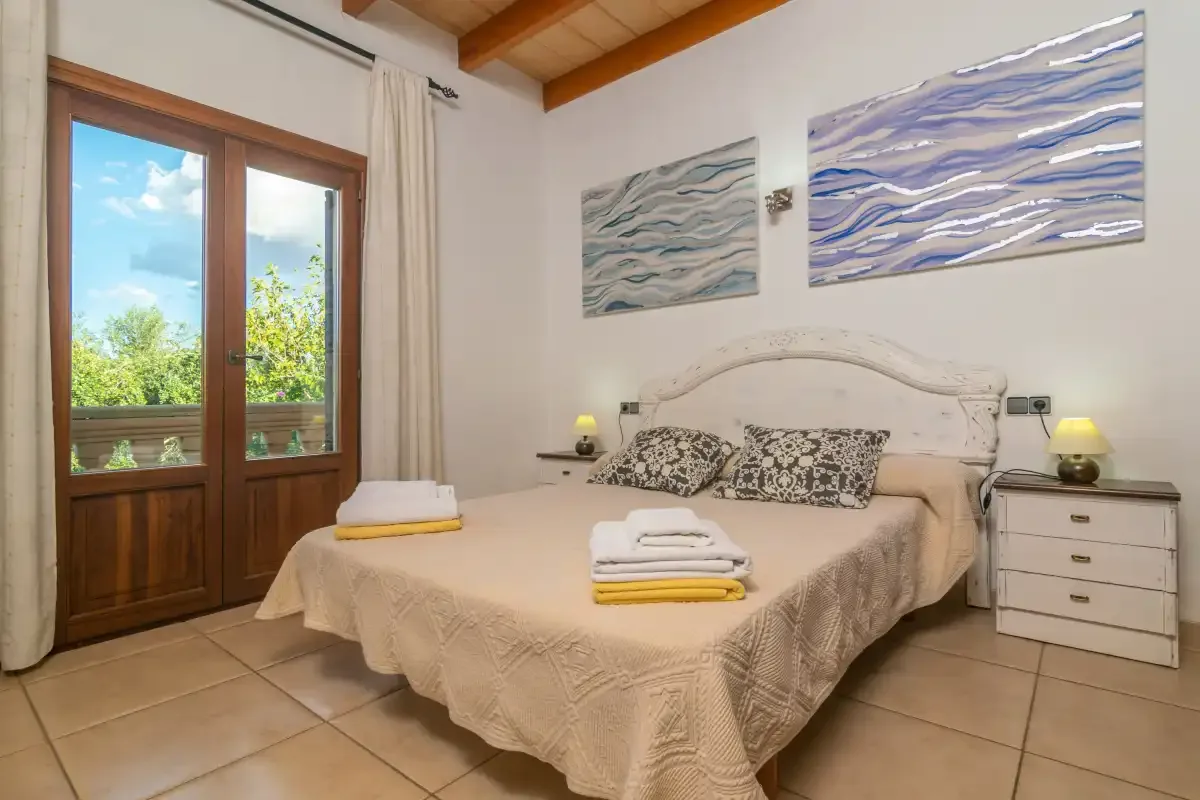A bedroom with a bed, folded towels, and wooden balcony doors.