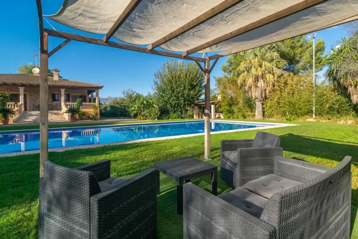 Outdoor seating beneath a canopy overlooks a swimming pool and landscaped garden.