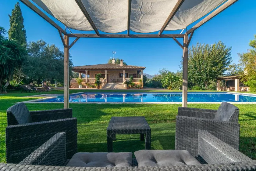 Asientos al aire libre bajo un toldo con vistas a una piscina y un césped.