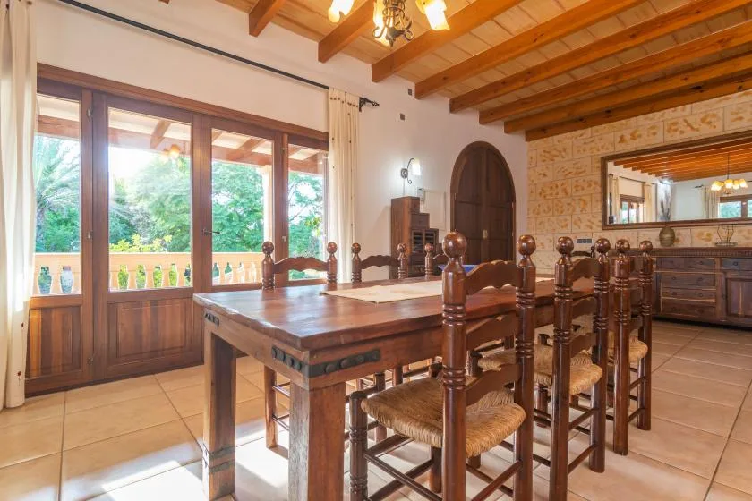 A dining room with a large wooden table and chairs beside bright windows.