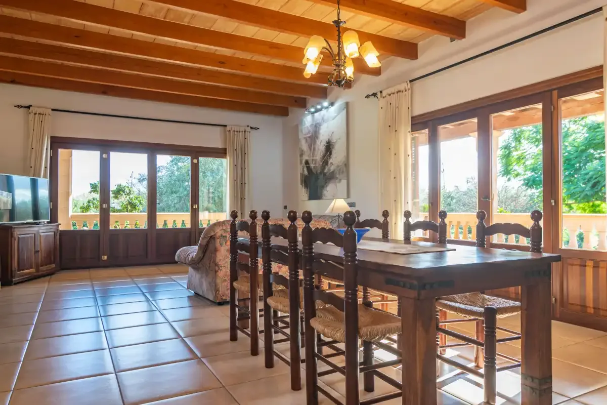 A dining area with a wooden table and chairs beside large windows.