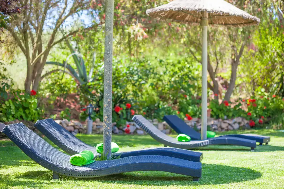 A garden seating area with lounge chairs beneath a thatched parasol.