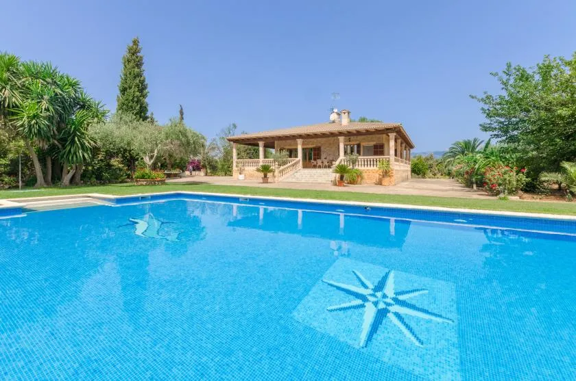 A swimming pool with a star-shaped tile design sits in front of a covered patio.