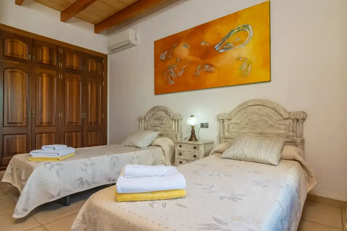 A bedroom with two beds, wooden wardrobes, and a bedside table.