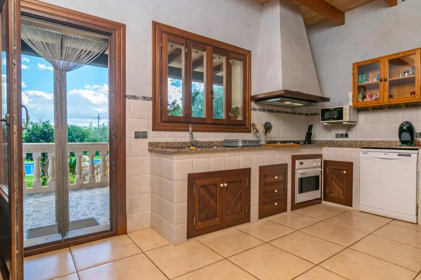 A tiled kitchen with wooden cabinets and a glass door opening onto a balcony.