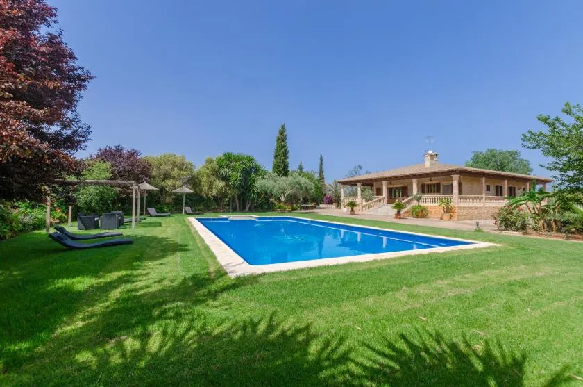 A swimming pool sits in a grassy garden beside a low house.