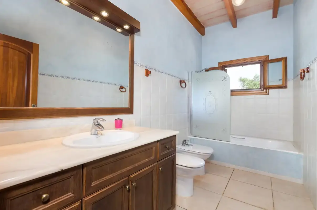 A tiled bathroom with a vanity, mirror, toilet, and bathtub.