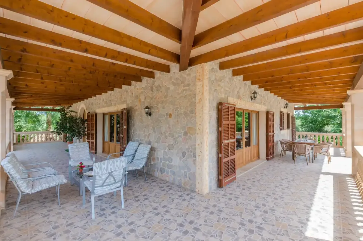 A covered stone patio with wooden ceiling beams and outdoor seating.