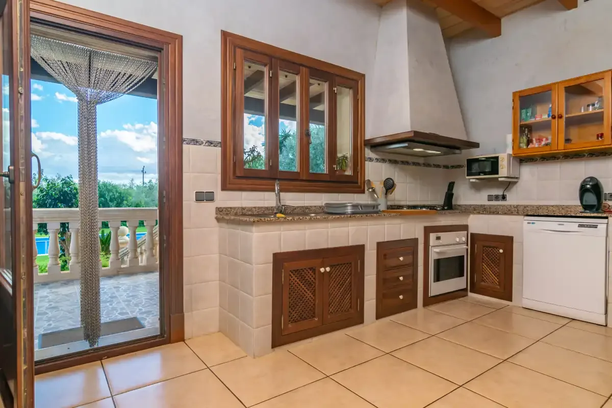A tiled kitchen with wooden cabinets and a glass door opening onto a terrace.