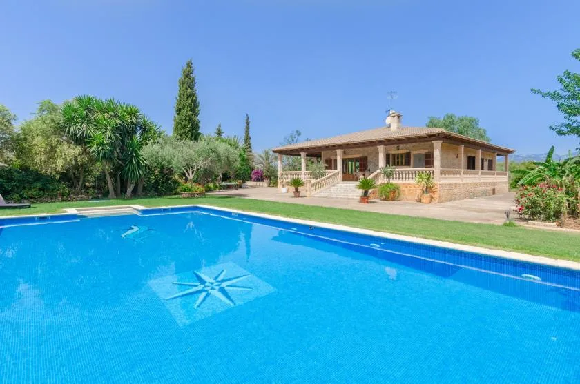 A swimming pool in front of a single-story house, surrounded by greenery.