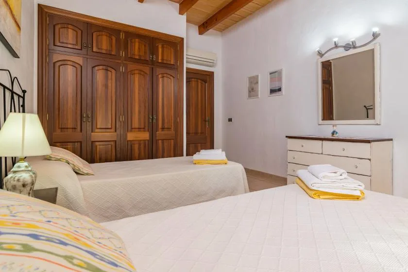 A bedroom with two beds, a wooden wardrobe, and a dresser beneath a mirror.