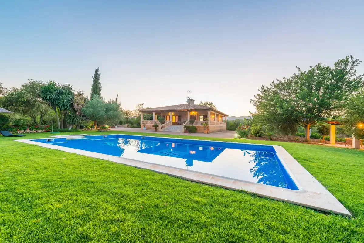 An outdoor swimming pool sits on a lawn in front of a single-story house.