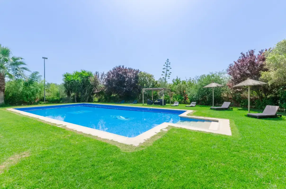 A swimming pool sits in a sunny garden with loungers and umbrellas.