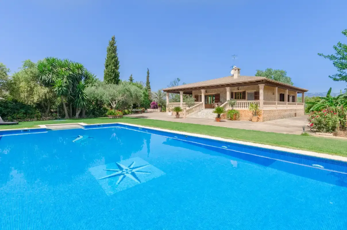 An outdoor swimming pool sits in front of a single-story house and garden.