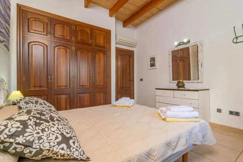 A bedroom with a bed, wooden wardrobes, and a dresser topped by a mirror.