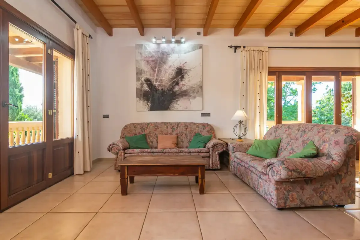 A living room with patterned seating, a wooden coffee table, and exposed ceiling beams.