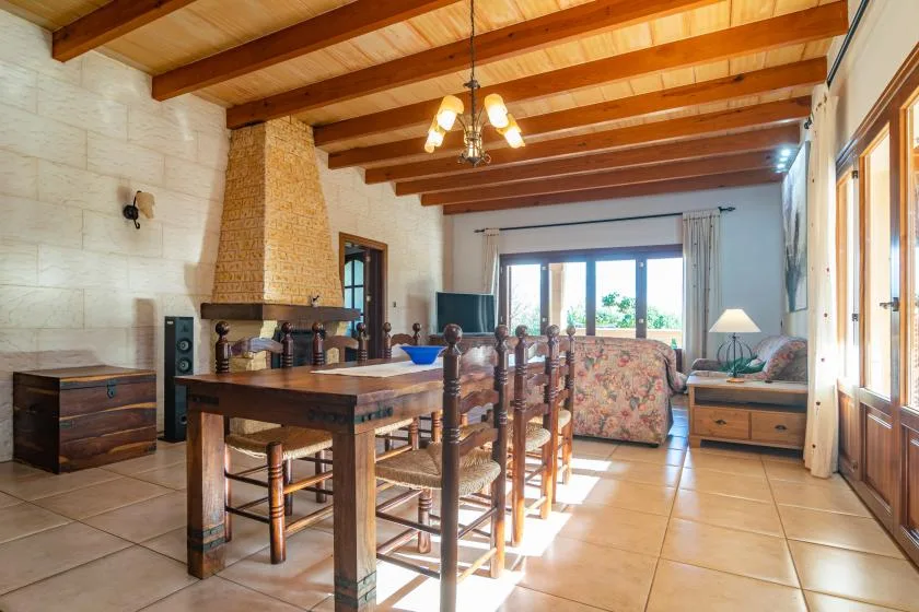 A dining and living area with a wooden table and seating beside large windows.