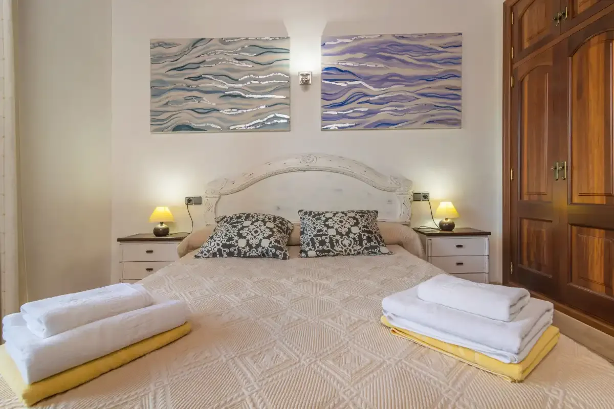 A bedroom with a neatly made bed and folded towels.