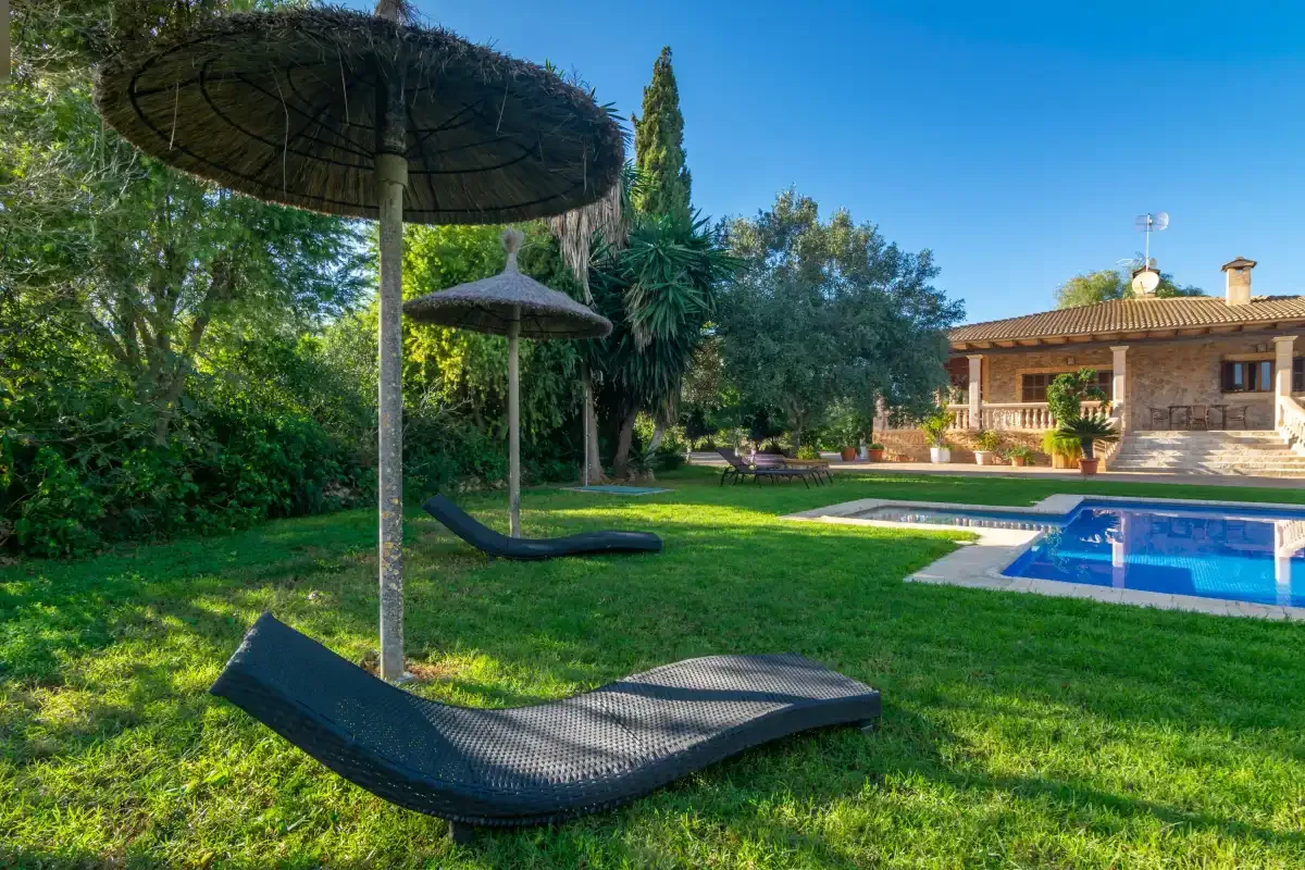 A garden pool area with lounge seating and a stone house in the background.