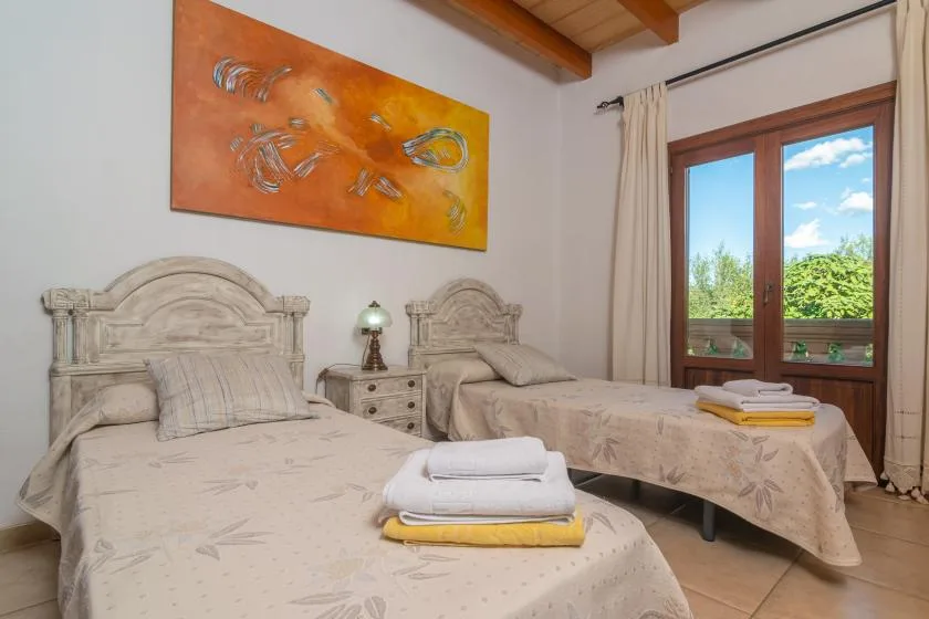 A twin bedroom with two beds, folded towels, and a window overlooking greenery.