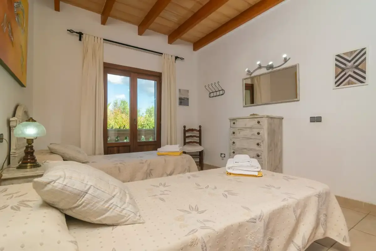 A bedroom with beds, a window, and exposed wooden ceiling beams.