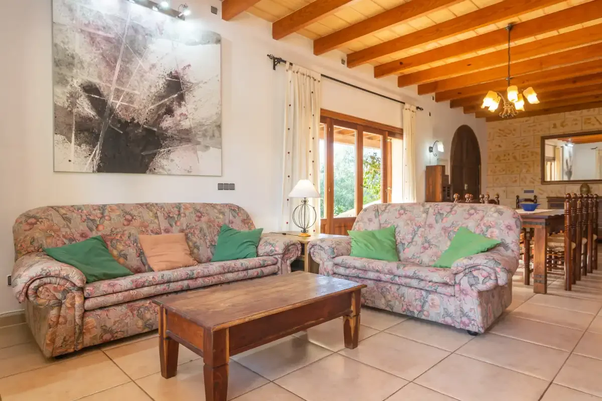 A living room with floral seating, a wooden coffee table, and exposed ceiling beams.
